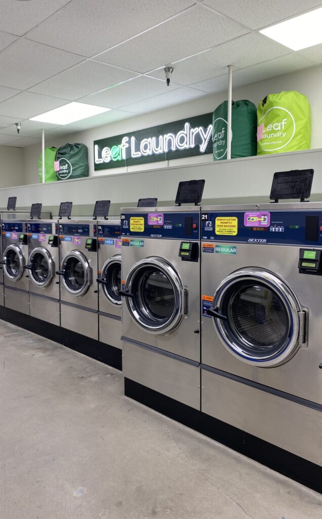 Row of commercial washers with four Leaf Laundry bags above